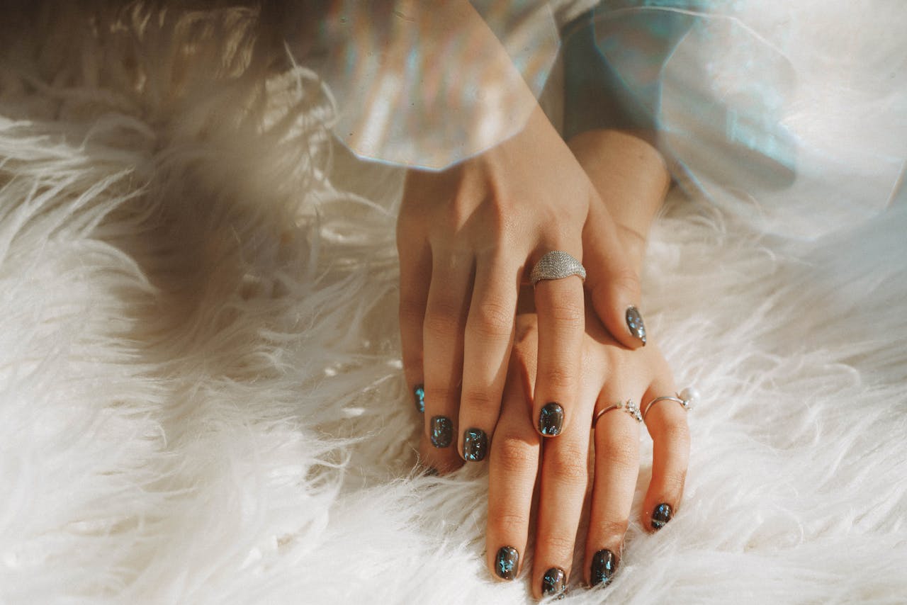 Close-up of a womans hands wearing rings and nail art, resting on white faux fur.